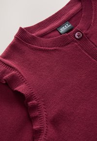 Bordeauxrode gebreide cardigan met een ronde halslijn, voorzien van ruches langs de schouder en een enkele knoopsluiting.