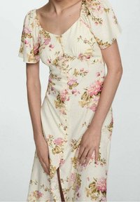 Robe florale en tissu jaune clair, ornée de fleurs roses, avec des manches bouffantes courtes, un devant à boutons et une fente sur le côté pour plus de détails.