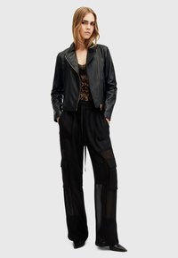 Zwarte leren bikerjack over een kanten cami, gecombineerd met zwarte doorschijnende cargobroek. Outfit heeft lange mouwen en schoenen met puntige neus.