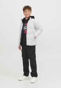 Ljusgrå puffjacka med huva, dragkedjestängning, två sidofickor, kombinerad med en svart huvtröja och mörka cargobyxor, avslutad med vita sneakers.