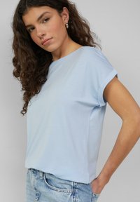 Lichtblauw T-shirt met korte mouwen van zachte stof, met een relaxed fit en opgerolde mouwen, gecombineerd met licht denim jeans.