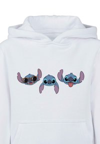 Felpa bianca con cappuccio che presenta tre volti di personaggi dei cartoni animati: uno con occhiali da sole, uno neutro e uno con la lingua di fuori. Tessuto morbido.