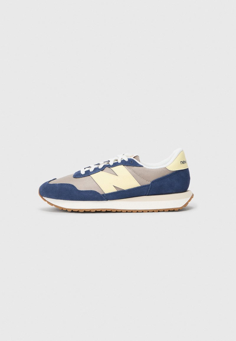 Sneakers met een marineblauwe suède bovenkant, beige gaas en crèmekleurige accenten. Voorzien van witte veters en een gumrubberen zool. "New Balance" logo op de hak.
