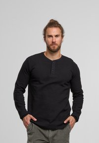 Schwarzes Langarm-Henley-Shirt mit gerippter Textur, ausgestattet mit einer Fünf-Knopf-Leiste und Rundhalsausschnitt. Getragen mit olivfarbenen Cargo-Hosen.