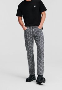 Jeans grises con patrón, de corte recto y con bolsillos frontales visibles, combinados con una camiseta negra de manga corta y botas negras gruesas.