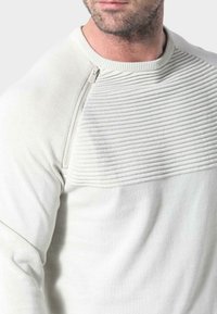 Hellgraues Sweatshirt mit geripptem Oberteil, Strickstruktur und Reißverschlussdetail an der Schulter. Glatter Körper mit sportlichem Schnitt.