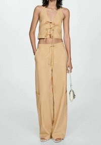 Beige zkrácený halter top s krajkovým detailem vpředu, kombinovaný s kalhotami širokého střihu, které mají kapsy. Materiál vypadá lehce a hladce.