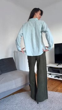 Blusa azzurro chiaro con pois in rilievo, maniche lunghe e spalline posteriori, abbinata a pantaloni a zampa d'elefante in velluto a coste verde oliva. Tessuto piatto e vestibilità casual.