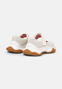 Zapatillas blancas con suela de goma, con una cinta de velcro y un cuello acolchado, mostradas desde la parte trasera sobre un fondo liso.