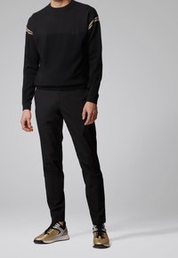 Maglione nero con accenti a righe, pantaloni neri e sneakers con dettagli dorati. I materiali sono in maglia e tessuto con una finitura testurizzata.