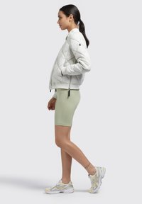Padded bomber jacket in light gray, featuring a quilted design and side zipper. Paired with mint green cycling shorts and white sneakers with yellow accents.