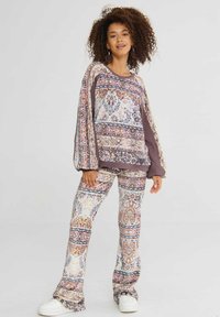 Geprinte loungewear set met een oversized top in pastelkleuren met bruine accenten en bijpassende flared broek; de stof is soepel.