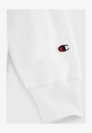 Polsino di felpa bianca con texture a coste, caratterizzato da un piccolo logo ricamato con accenti rossi e neri. Tessuto liscio con cuciture pulite.