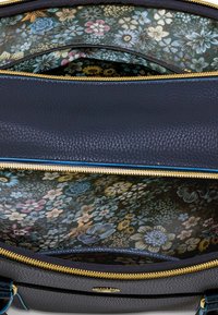Navy leather bag interior features a floral-patterned lining in shades of blue, pink, and yellow, with gold zipper detailing.