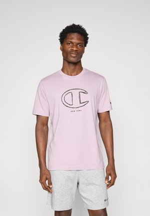 T-shirt en coton violet clair avec un logo noir et le texte "NEW YORK" centré sur le devant. Manches courtes et col rond.