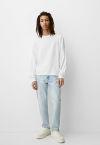 Tricou alb cu mânecă lungă, blugi albaștri deschis și sneakers albi. Croială casual, textură moale, design relaxat. Estetic simplu și minimalist.