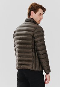 Ciemnobrązowa kurtka puchowa z pionowymi przeszyciami, wysokim kołnierzem i gładką, błyszcząca teksturą. Zaprojektowana z myślą o ciepłości i komforcie.