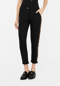 Pantaloni neri in materiale elasticizzato, con stampa leopardata lungo i lati, orli arrotolati e chiusura frontale con bottone.