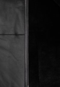 Zwarte leren jas met ritsluiting, met een gladde buitenkant en een zachte, gestructureerde binnenkant. De panelen hebben stijlvolle stikseldetails.