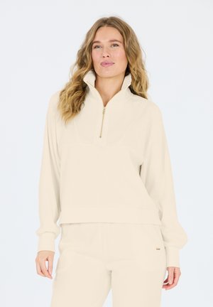 Light beige ribbed quarter-zip sweatshirt with a high collar, featuring a gold zipper and relaxed fit. Soft fabric, long sleeves.