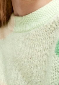 Primer plano de una persona que lleva un suave suéter de punto verde claro con un cuello acanalado y textura de punto visible.