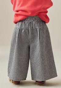 Pantaloni a gamba larga in gessato bianco e nero con cintura elastica. Il tessuto sembra leggero e texturizzato. Sono visibili delle scarpe marroni.