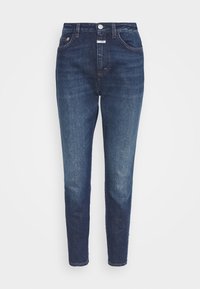 Jean en denim délavé foncé avec une jambe fuselée, une taille haute, cinq poches et une braguette à glissière. Présente des coutures contrastantes et une finition soignée.