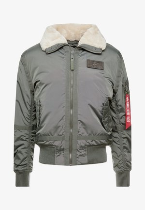 Groene bomberjack met een zachte beige nepbont kraag, ritssluiting, elastische manchetten en een rood label met de tekst "VERWIJDER VOORDAT JE VLIGT."