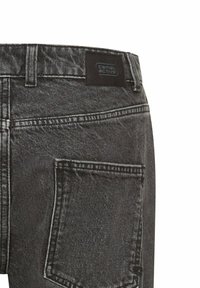Black denim jeans featuring a high waistband, visible stitching, and a back pocket. Logo patch on the waistband. Textured fabric.
