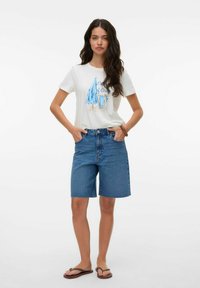 Camiseta blanca con gráfico azul de sillas de playa, combinada con pantalones cortos de mezclilla de un azul claro y chanclas marrones. Atuendo de verano simple y casual.