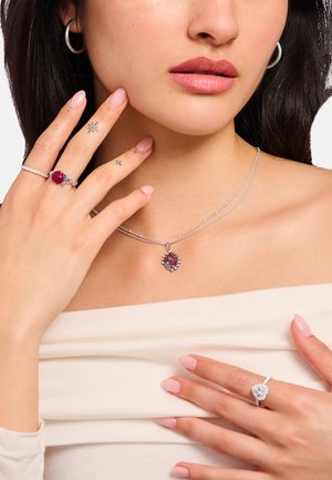 Silberschmuck mit einem Rosenanhänger an einer Lagenkette, einem Blumenring und einem funkelnden Ring; alle mit polierter Oberfläche.