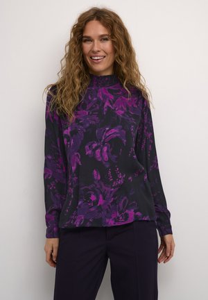 Blouse à manches longues avec un motif floral dans des nuances de violet sur un fond sombre, dotée d'un col haut et d'un tissu texturé.