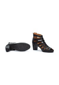 Sandalias de tacón de cuero negro con tiras recortadas, punta abierta y suela texturizada. Los tacones son de forma cuadrada con un acabado suave.