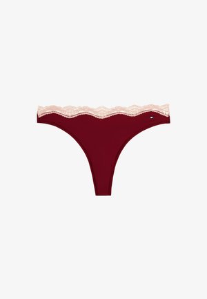 Tanga burdeos con una cinturilla de encaje en rosa claro, que presenta un borde en forma de onda y una pequeña etiqueta con logo en el costado. Textura de tela suave.