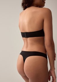 Czarny top bikini typu bandeau z zapięciem na zatrzask, w połączeniu z dopasowanymi czarnymi majtkami o niskim stanie. Gładki, elastyczny materiał o minimalnym stopniu krycia.