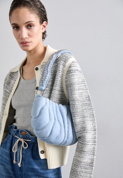 Fyldig lyseblå håndtaske med bølget struktur, med en vævet rem med stjerneaccenter, parret med en grå cardigan og denim.