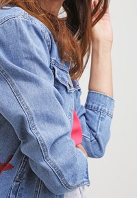 Džínová bunda v světle modrém odstínu, s klasickým zapínáním na knoflíky a mírně zkráceným střihem. Měkká textura a viditelné detailní švy.