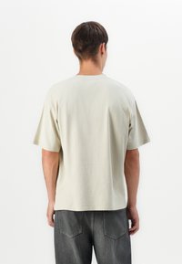 Beige bomulds T-shirt med korte ærmer, rund halsudskæring, afslappet pasform og en glat overflade, kombineret med mørkegrå bukser.