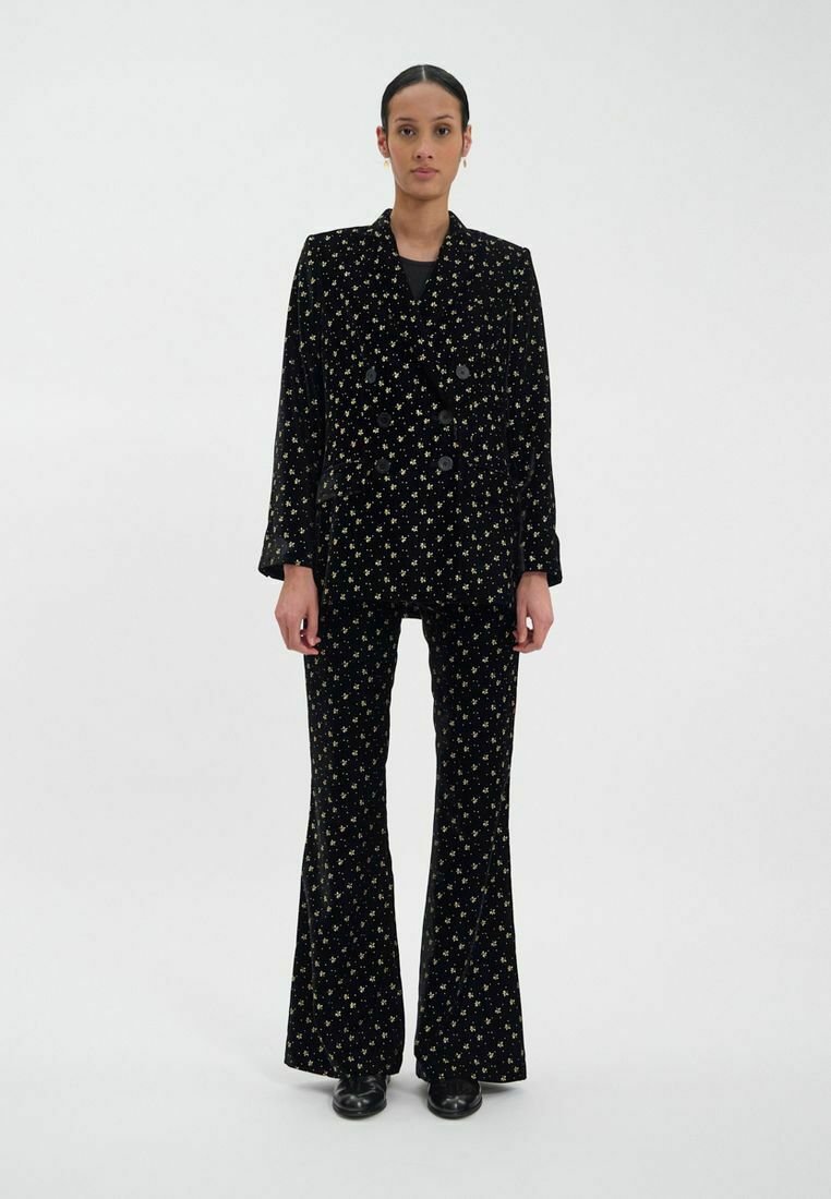 Costume en velours noir avec un motif d'étoiles dorées, comprenant un blazer croisé et un pantalon évasé. Texture lisse, coupe ajustée.