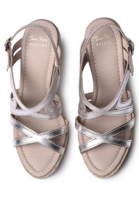 Sandalias plateadas metálicas con tiras, un acabado acolchado en color beige, que cuentan con tiras cruzadas y una suela texturizada. Hebilla ajustable en el tobillo.