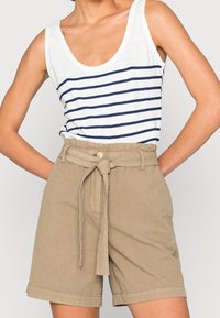 Weißes Tanktop mit marineblauen Streifen, kombiniert mit hellbraunen, hoch taillierten Shorts mit gebundenem Stoffgürtel und umgeschlagenem Saum.