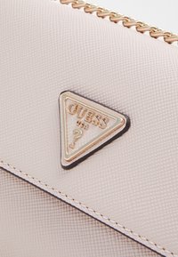 Ljusrosa texturerad konstläderhandväska med en triangulär guldfärgad logotypplakett, med guldkedjeaccenter och kontrastsömmar.