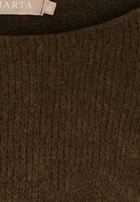 Nära bild av mörkbrun ribbad stickad tyg med en delvis synlig beige klädlapp sydd vid halslinningen.