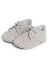 Scarpe in suede grigio con punta rotonda, suola piatta, cuciture dettagliate e perforazioni in stile brogue lungo i lati e la parte anteriore.