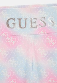 Rosa och blått tyg med en diamantmönster med vita logotyper, elastisk midja med silverfärgad "GUESS"-text. Slät textur.