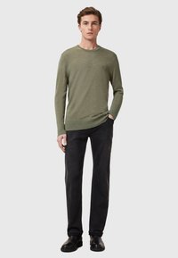 Olijfgroen lange mouwen trui met een ronde hals, slim fit en ribbels aan de cuffs, gecombineerd met donkere jeans en zwarte schoenen.
