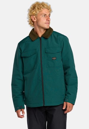 Teejacke in Teal mit einem Reißverschluss vorne, zwei Brusttaschen und einem braunen Fellkragen. Verfügt über ein dezentes Logopatch und eine lockere Passform.