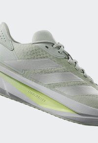Lichtgroene sportschoen van mesh en synthetisch materiaal. Heeft doorzichtige witte accenten en een lichtgroene tussenzool met het label "LIGHTMOTION."