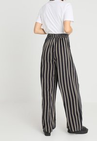 Černobílé proužkované kalhoty s širokým nohama a elastickým pasem. Hladká textilie. Noste s obyčejným bílým tričkem a černou obuví.