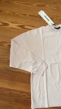 Camicia bianca a maniche lunghe con polsini a costine posta su un pavimento in legno, con un'etichetta bianca con il marchio "PEGADOR" attaccata vicino al colletto.